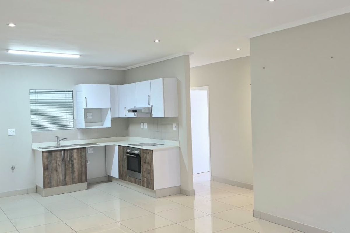 A clean, open-plan kitchen featuring modern two-tone cabinetry, built-in oven, extractor fan, and tiled flooring, offering a functional and bright workspace.