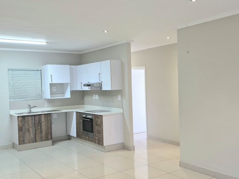 A clean, open-plan kitchen featuring modern two-tone cabinetry, built-in oven, extractor fan, and tiled flooring, offering a functional and bright workspace.