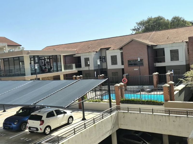 Exterior view of the apartment complex featuring a swimming pool, covered parking area, and well-maintained brick and masonry building facades.