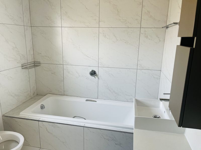 Modern bathroom featuring a built-in bathtub, wall-mounted basin, and elegant marble-look wall tiling throughout.