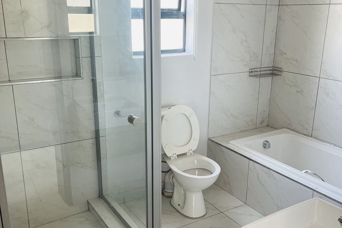 Modern bathroom featuring a glass shower enclosure, built-in shower niche, bathtub, and vanity basin with contemporary marble-look tiling throughout.