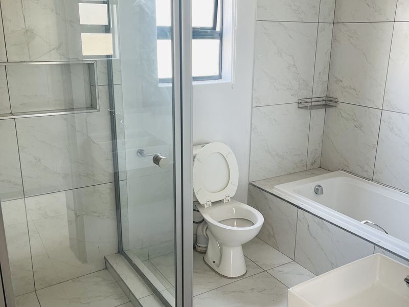 Modern bathroom featuring a glass shower enclosure, built-in shower niche, bathtub, and vanity basin with contemporary marble-look tiling throughout.