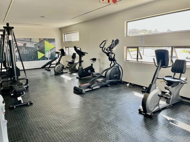 A well-maintained gym facility featuring durable rubber flooring, multiple horizontal awning windows for natural light, and recessed ceiling lighting.