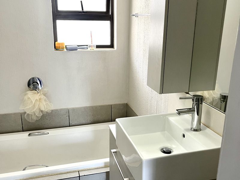 A compact, modern bathroom featuring a bathtub, a contemporary square basin with a vanity cabinet, and neutral grey floor and wall tiling.