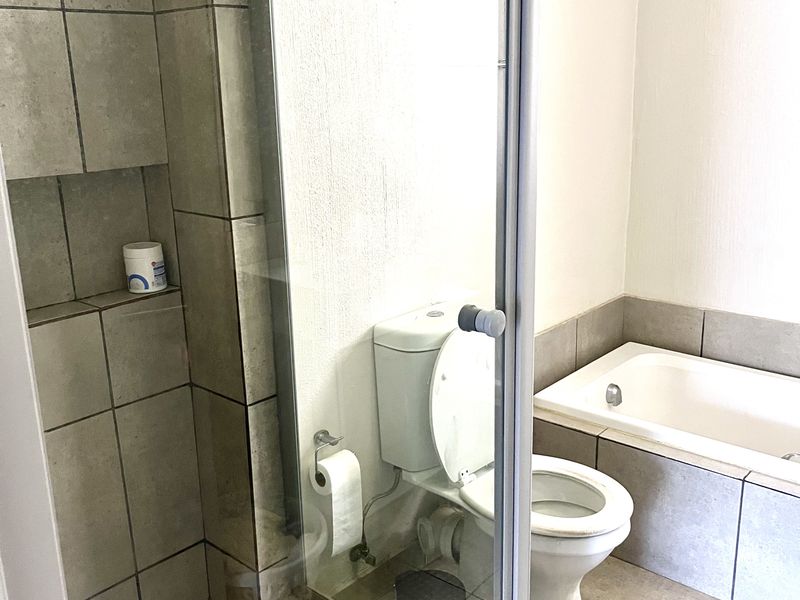 A functional bathroom featuring a glass-enclosed shower with built-in niche, a standard toilet, and a tiled bathtub surround.