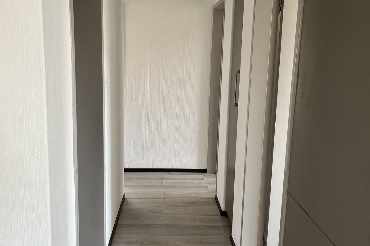 A clean, empty hallway featuring light-toned laminate flooring and neutral wall finishes, providing access to multiple rooms within the apartment.