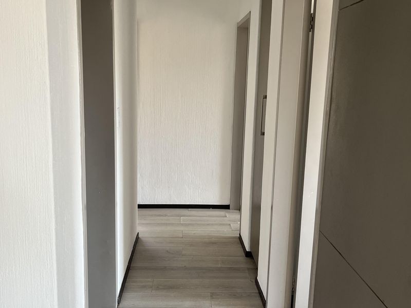A clean, empty hallway featuring light-toned laminate flooring and neutral wall finishes, providing access to multiple rooms within the apartment.