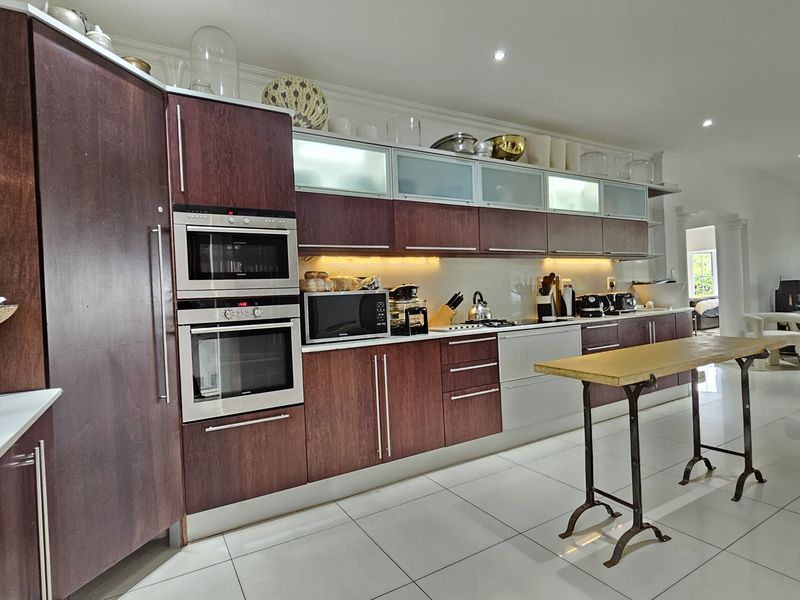 Modern kitchen featuring dark wood cabinetry, integrated appliances, sleek tiled flooring, and recessed lighting, flowing into an open-plan living area.