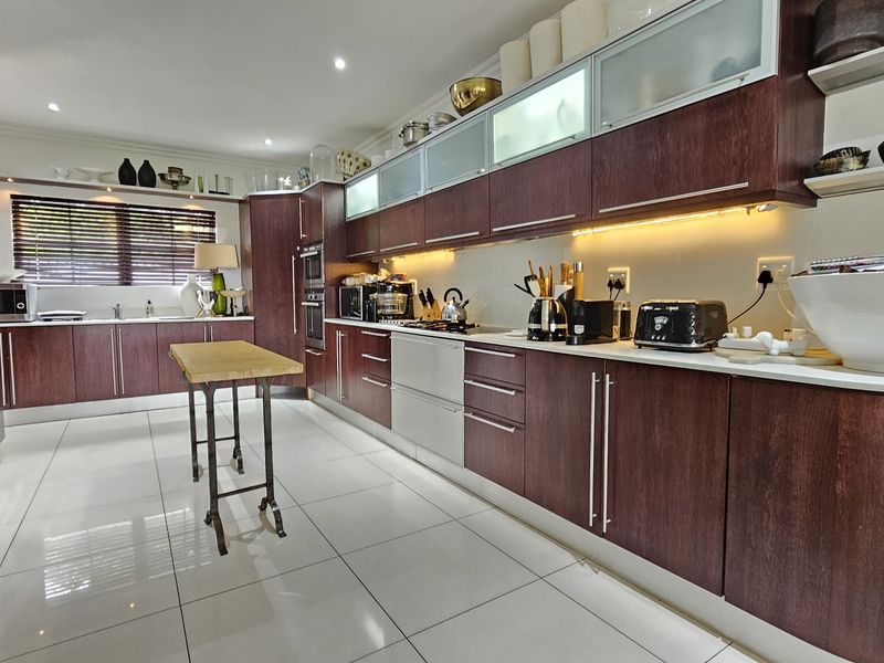 A spacious kitchen featuring dark wood cabinetry, under-cabinet lighting, tiled floors, and integrated appliances, offering a functional and well-lit culinary workspace.