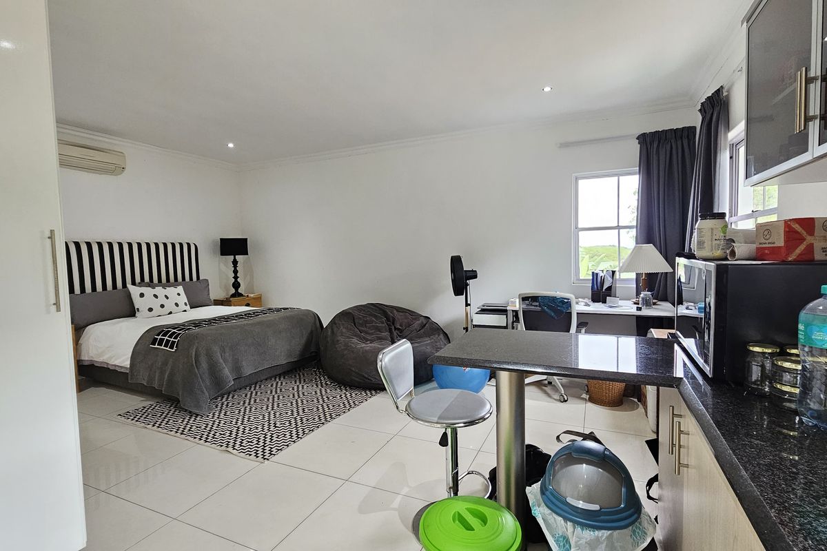 A spacious bedroom featuring tiled flooring, a split-system air conditioner, and a built-in kitchenette area with granite countertops.