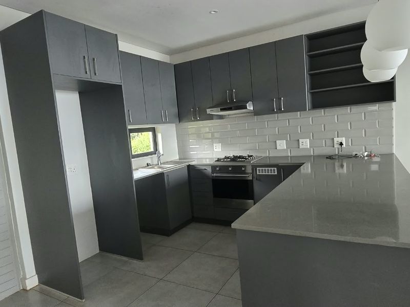 Modern kitchen featuring dark grey cabinetry, stone countertops, subway tile backsplash, built-in oven, gas hob, and a functional kitchen island.