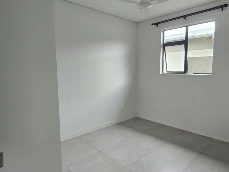 A clean, empty bedroom featuring neutral tiled flooring, a ceiling fan, and a window with a black frame.