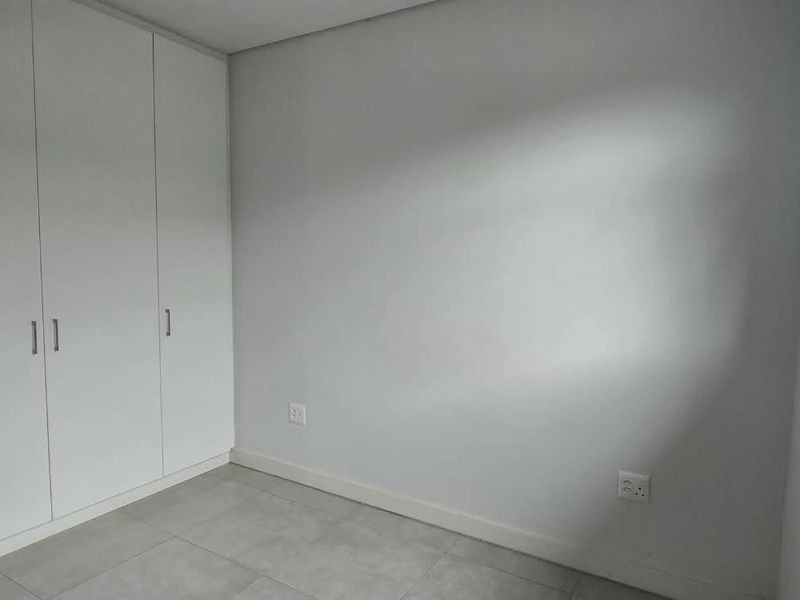 A clean, empty bedroom featuring neutral tiled flooring, built-in white cupboards, and a window providing natural light.