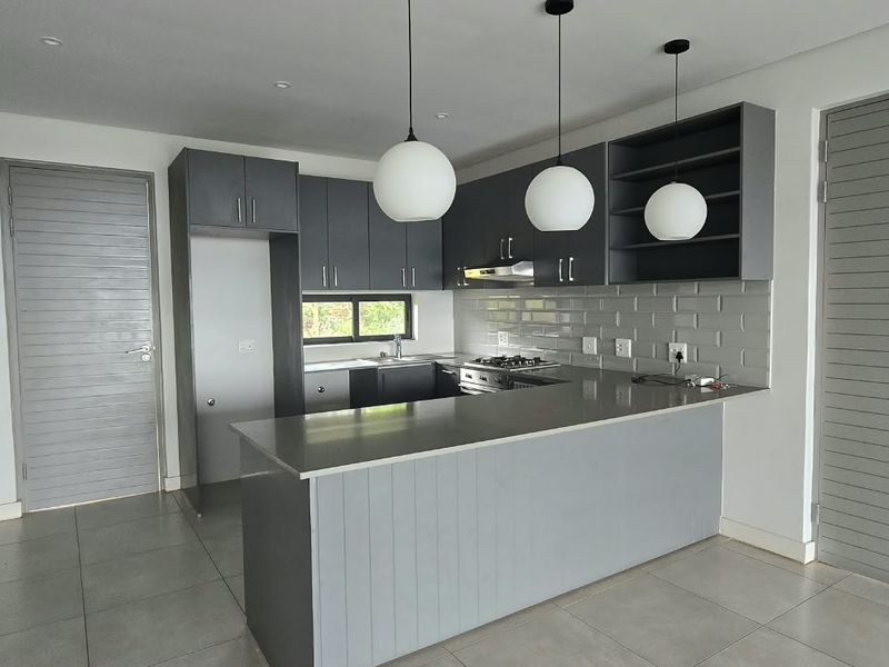 Modern kitchen featuring grey cabinetry, subway tile backsplash, stone countertops, gas hob, extractor fan, and contemporary pendant lighting.