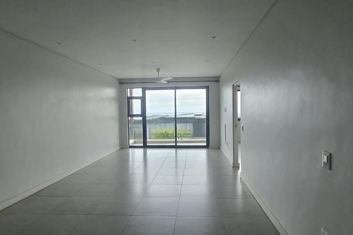 A spacious, empty living area featuring neutral tiled flooring, recessed lighting, and a large sliding glass door providing natural light and outdoor access.