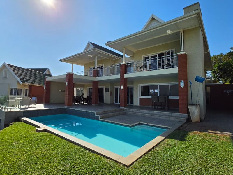 Rear view of a two-story house featuring a swimming pool, paved patio area, and an upper-level balcony with brick architectural detailing.