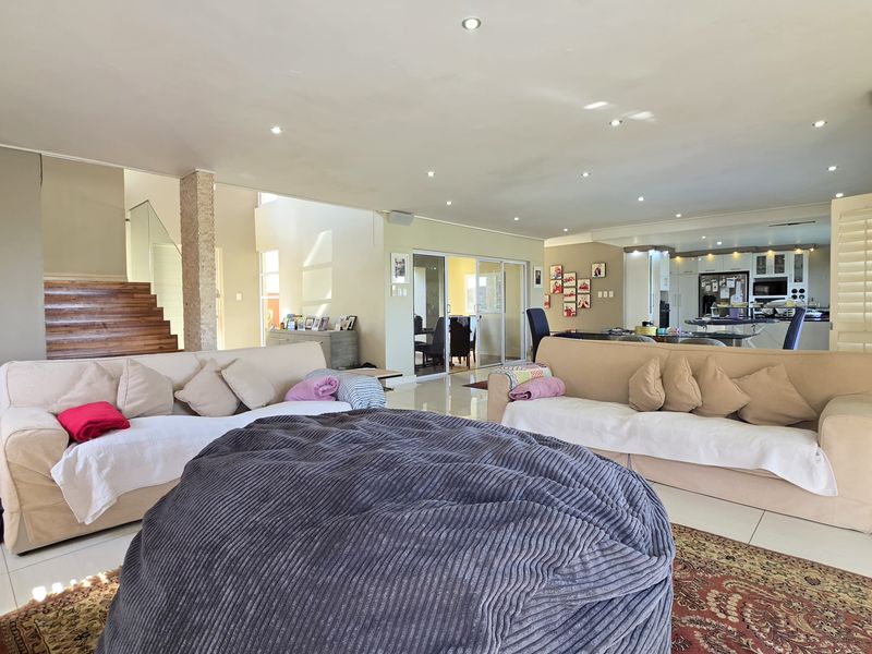 Spacious open-plan living area featuring tiled floors, recessed lighting, and a wooden staircase, seamlessly connecting to the kitchen and dining space.