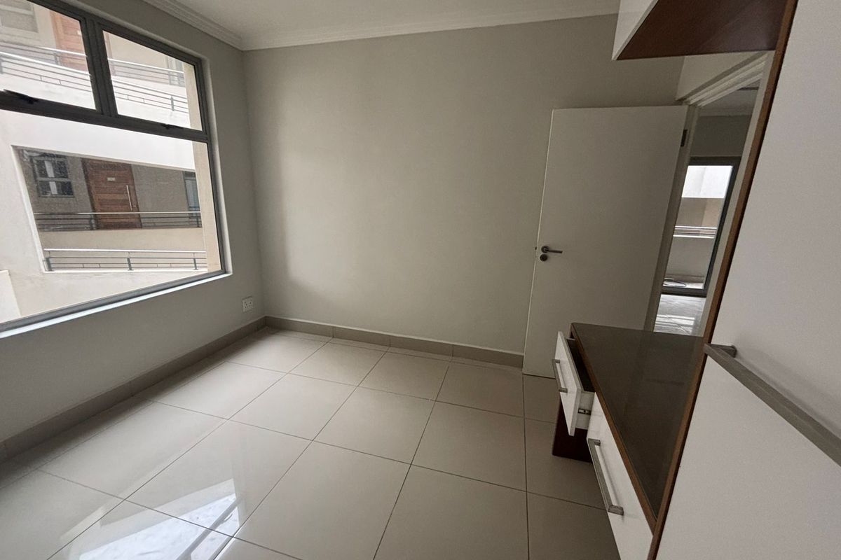A bright, empty bedroom featuring neutral tiled flooring, built-in cabinetry, and a large window providing natural light.