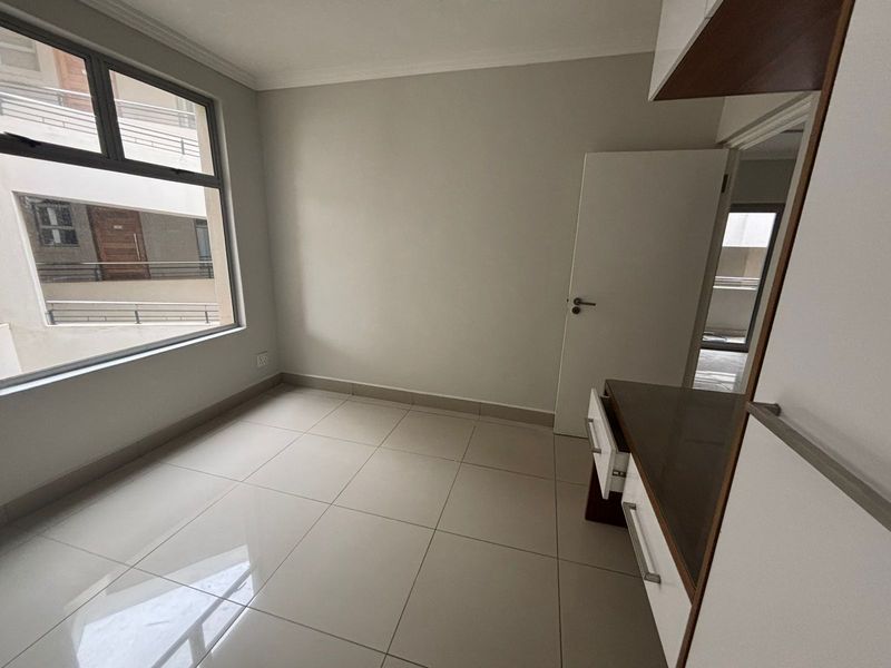 A bright, empty bedroom featuring neutral tiled flooring, built-in cabinetry, and a large window providing natural light.