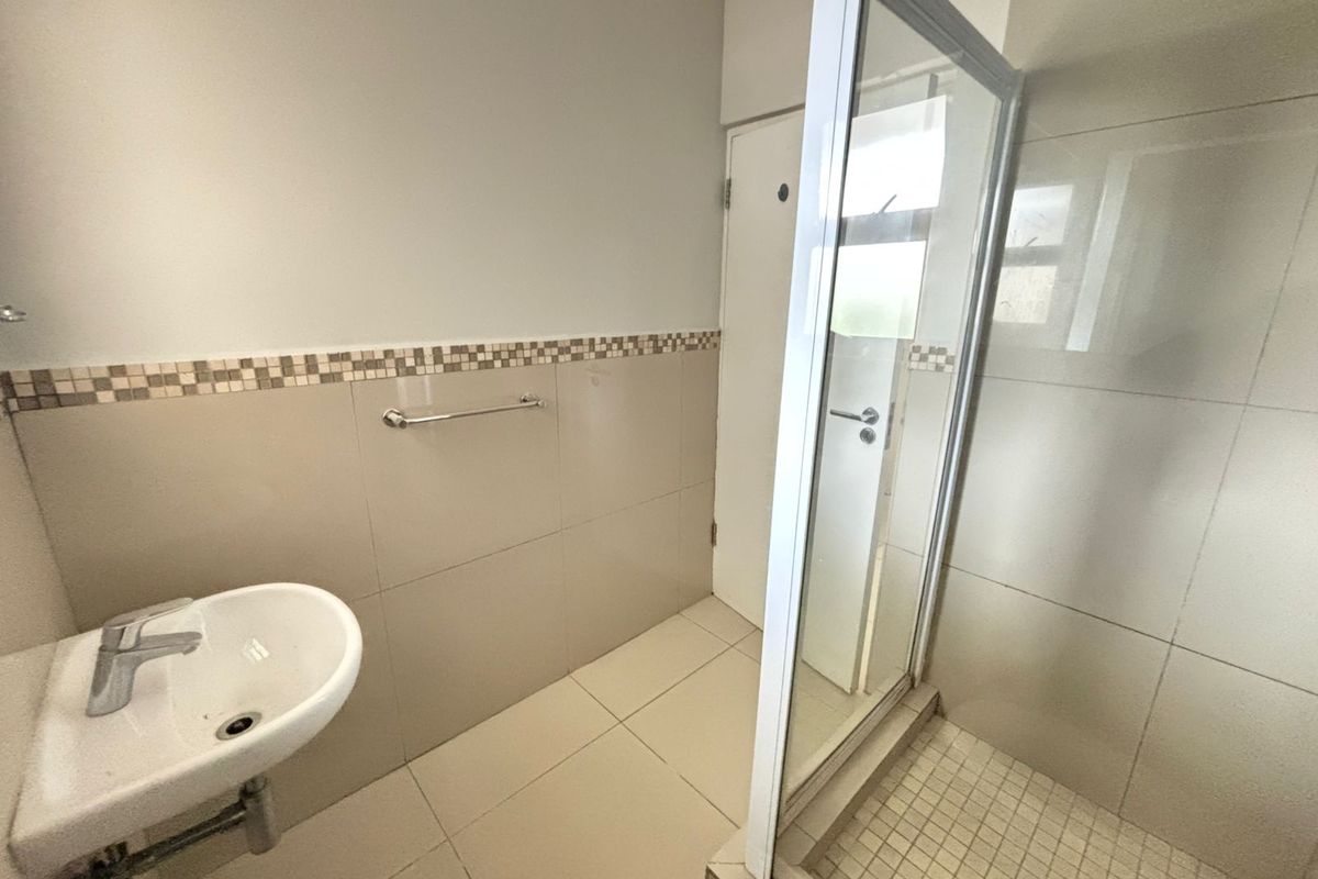 A clean, functional bathroom featuring a shower enclosure, wall-mounted basin, and neutral tiled finishes throughout.