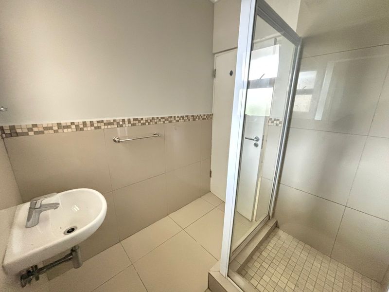 A clean, functional bathroom featuring a shower enclosure, wall-mounted basin, and neutral tiled finishes throughout.