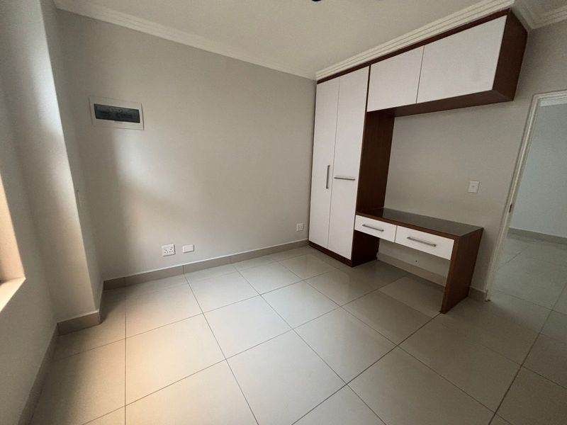 A clean, empty bedroom featuring neutral tiled flooring, modern built-in cabinetry with an integrated desk, and crisp white walls.