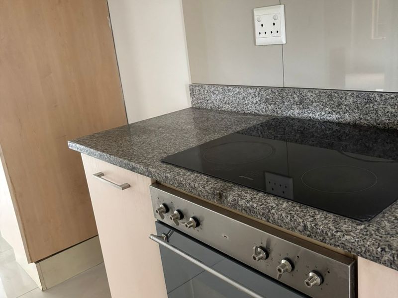A functional kitchen featuring granite countertops, built-in oven, electric hob, and light wood-finish cabinetry with tiled flooring.