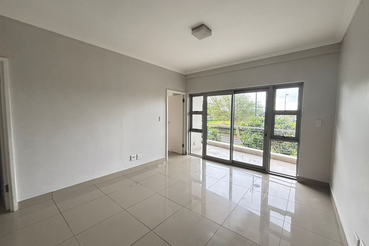 A bright, empty living room featuring neutral tiled flooring, clean walls, and a large sliding glass door providing access to an outdoor balcony.