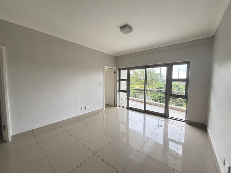 A bright, empty living room featuring neutral tiled flooring, clean walls, and a large sliding glass door providing access to an outdoor balcony.