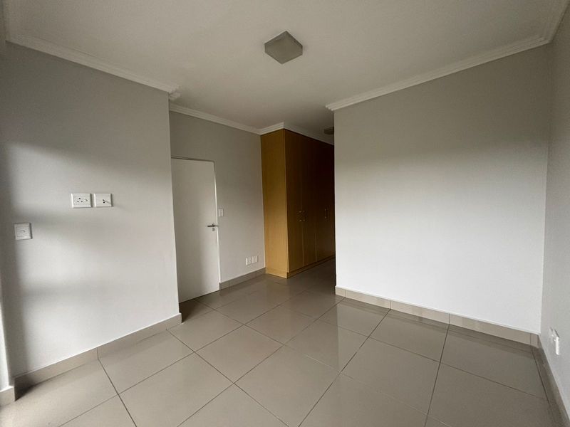A clean, empty bedroom featuring neutral wall paint, large format floor tiles, and built-in wooden cupboards with ample storage space.