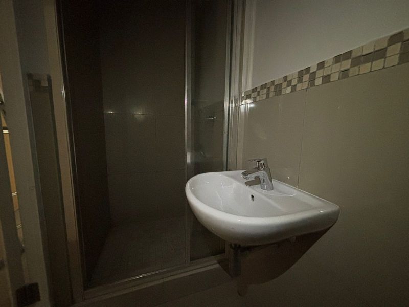 A functional bathroom featuring a wall-mounted basin with a chrome mixer tap and a separate shower enclosure with tiled walls.