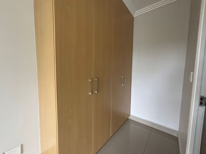A clean bedroom space featuring light wood-finish built-in wardrobes and neutral tiled flooring.