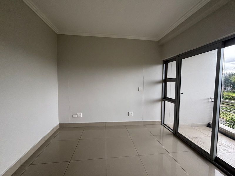 An empty, well-maintained living area featuring neutral tiled flooring, coving, and large sliding glass doors providing access to an outdoor balcony.