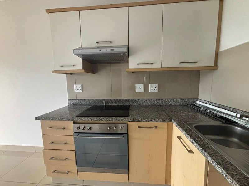 A clean, functional kitchen featuring granite countertops, built-in oven with electric hob, extractor fan, and ample laminate cabinetry for storage.