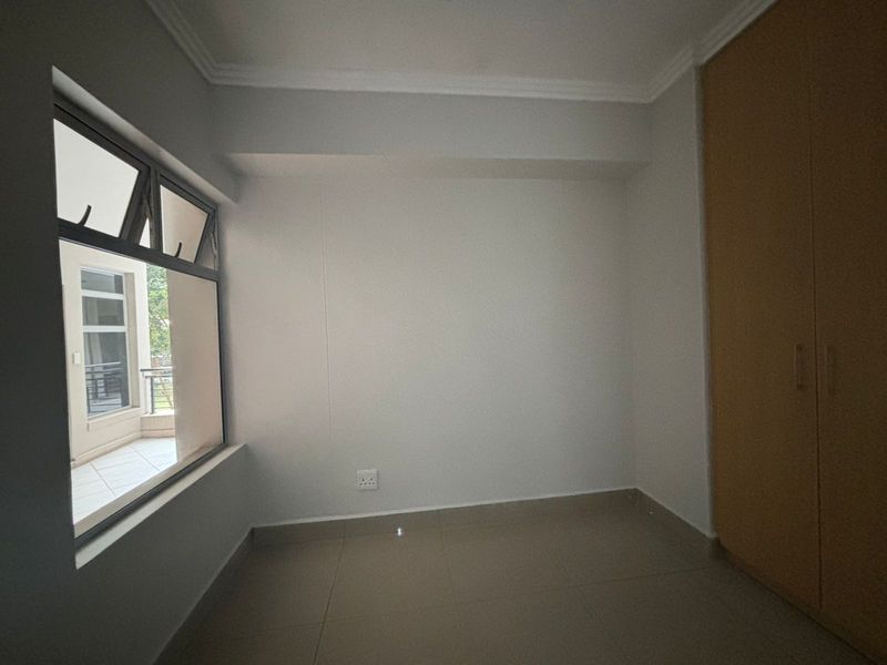 A clean, empty bedroom featuring neutral tiled flooring, a built-in wardrobe, and a large window providing natural light.
