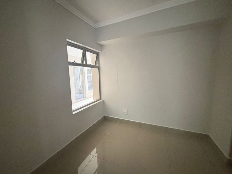 A clean, empty bedroom featuring neutral tiled flooring, white walls, and an aluminium-framed window, providing a blank canvas for personalization.
