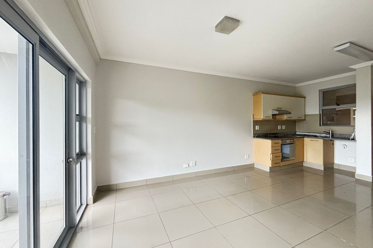 Open plan living area featuring tiled floors, a modern kitchen with granite countertops, built-in oven, and direct access to a balcony through sliding doors.