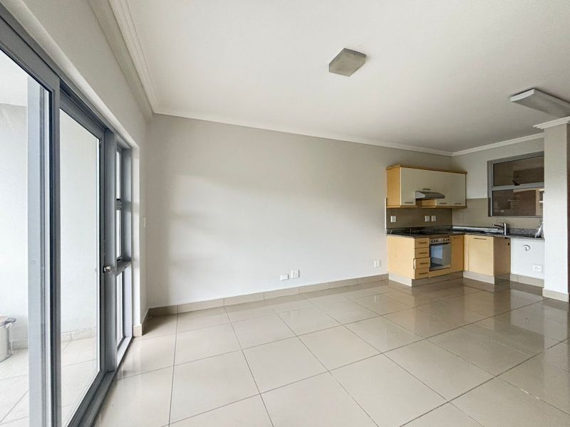 Open plan living area featuring tiled floors, a modern kitchen with granite countertops, built-in oven, and direct access to a balcony through sliding doors.