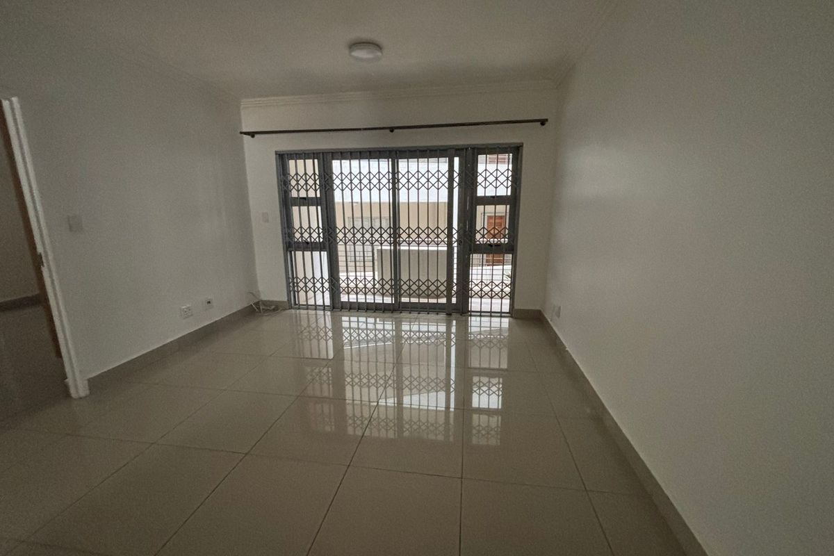An empty, well-maintained living area featuring neutral tiled flooring and a secure sliding door leading to an outdoor space.