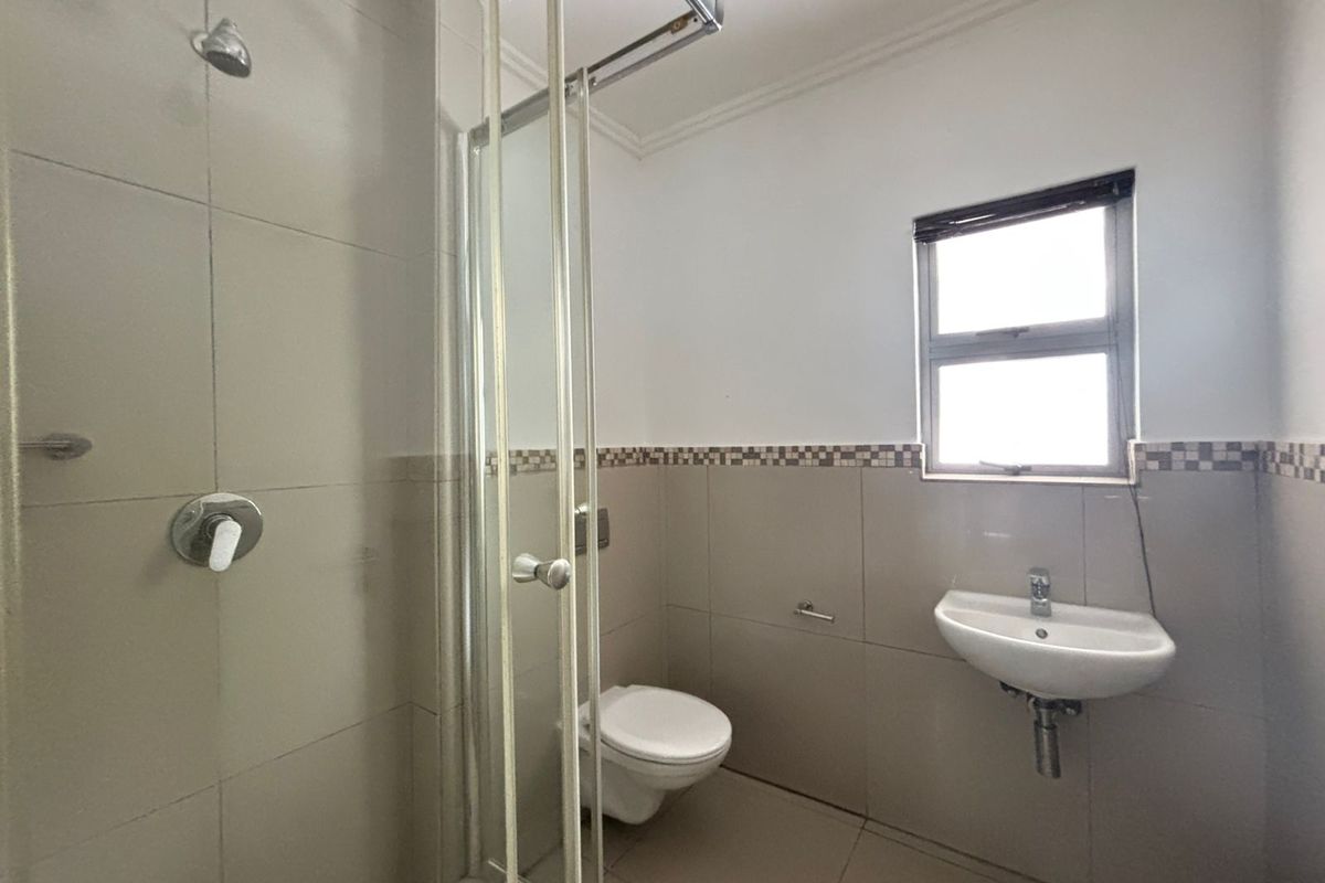 A functional bathroom featuring a glass shower enclosure, wall-mounted toilet, and basin with neutral wall and floor tiling.