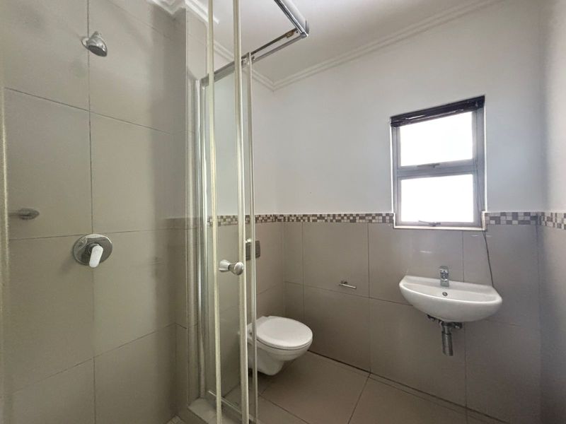 A functional bathroom featuring a glass shower enclosure, wall-mounted toilet, and basin with neutral wall and floor tiling.