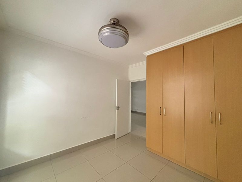 A clean, empty bedroom featuring neutral tiled flooring, built-in wooden cupboards, and a central ceiling light fixture.