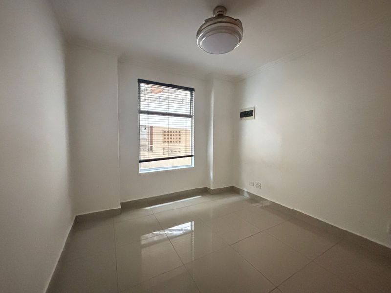 A clean, empty bedroom featuring neutral tiled flooring, a central ceiling light, and a window with fitted blinds.
