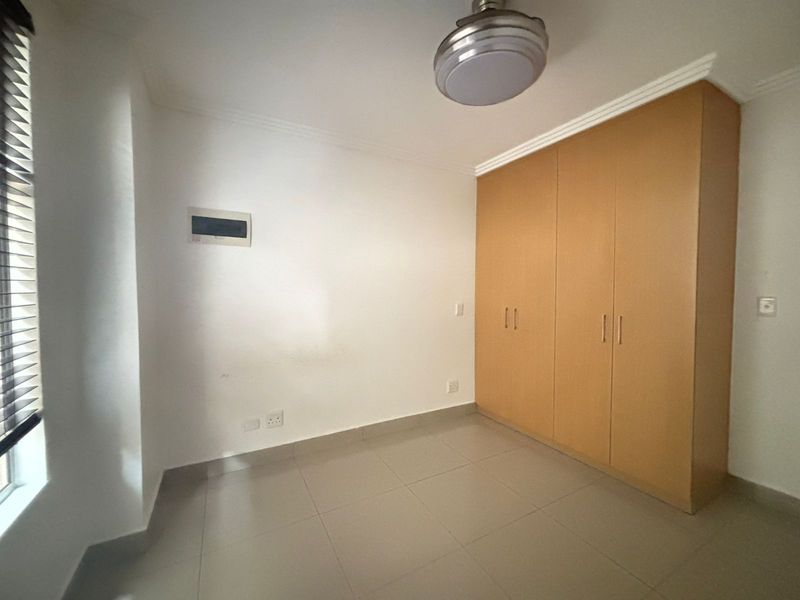 An empty bedroom featuring neutral tiled flooring, built-in wooden cupboards, a ceiling fan, and venetian blinds.