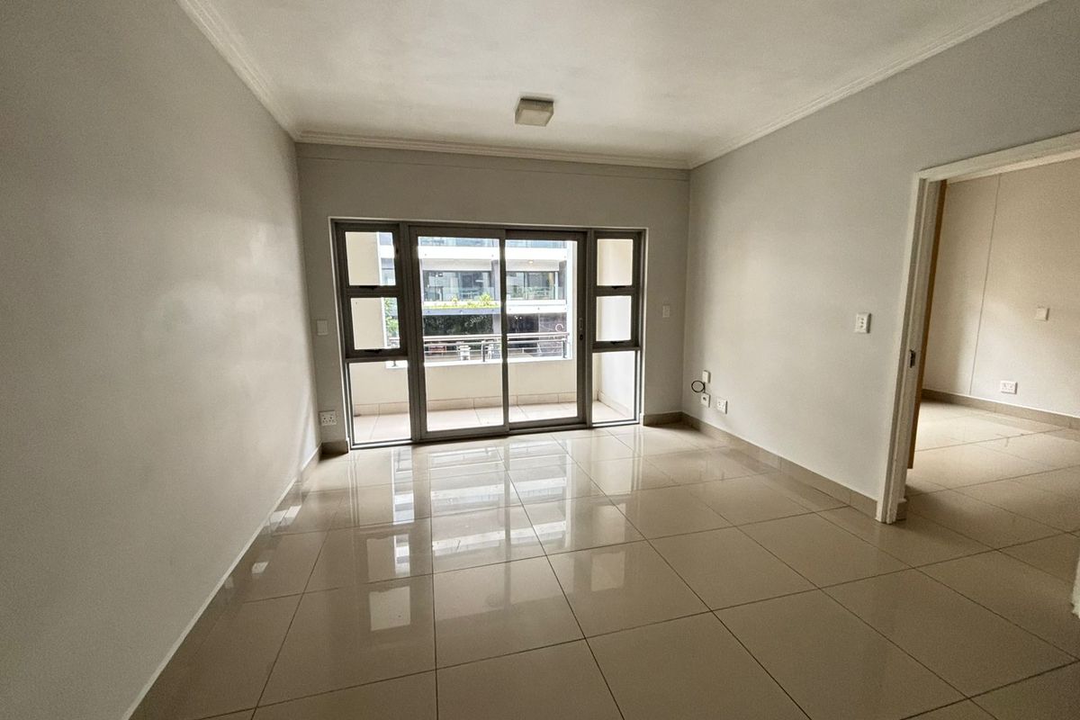 A bright, empty living room featuring neutral tiled flooring, a sliding glass door leading to a balcony, and clean, well-maintained wall finishes.
