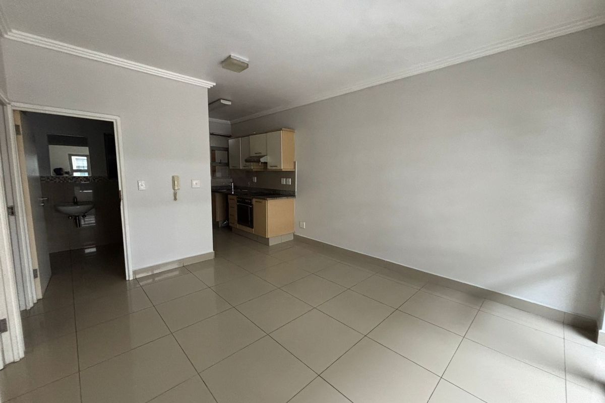 An open-plan living area featuring tiled flooring and a compact kitchen with built-in cabinetry, oven, and hob, leading to an adjacent bathroom.