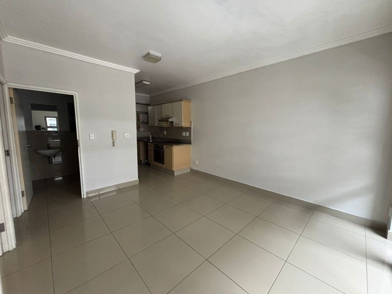 An open-plan living area featuring tiled flooring and a compact kitchen with built-in cabinetry, oven, and hob, leading to an adjacent bathroom.