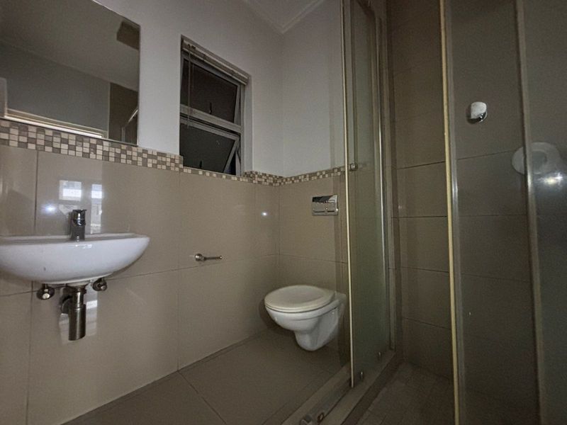 A functional bathroom featuring a wall-mounted toilet, a glass shower enclosure, and a wall-mounted basin with neutral tiled finishes.