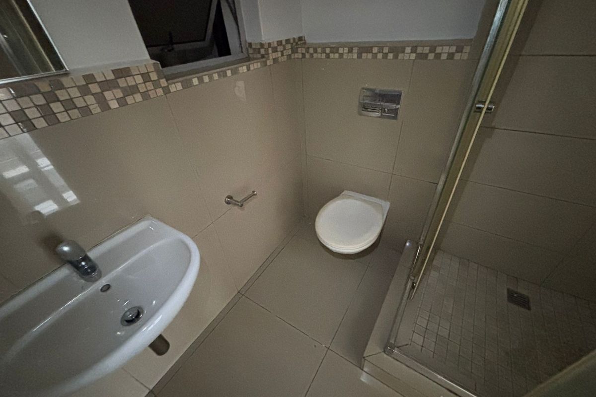 A functional bathroom featuring a wall-mounted basin, wall-hung toilet, and a glass-enclosed shower with neutral tiled finishes and a decorative mosaic border.