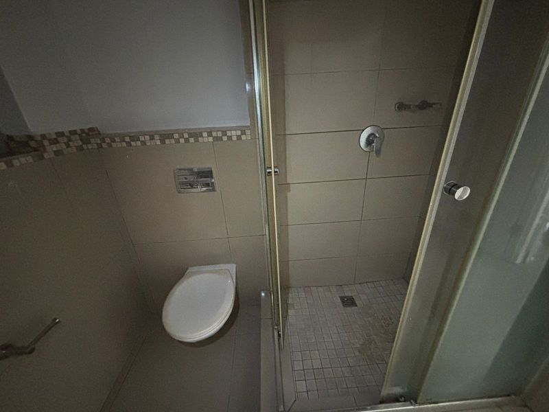 A compact bathroom featuring a wall-mounted toilet and a glass-enclosed shower with neutral ceramic tiling.